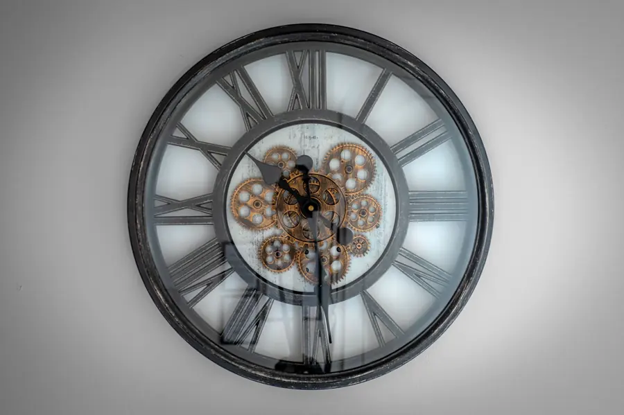Wall clock with Roman numerals and exposed brass gears visible behind the hands